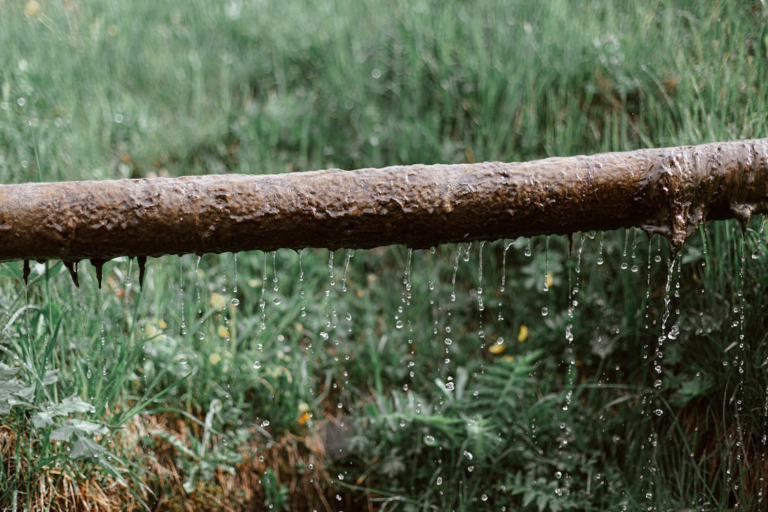 Corroded pipe leaking water onto grass, an example of a residential plumbing issue in Spokane, WA.