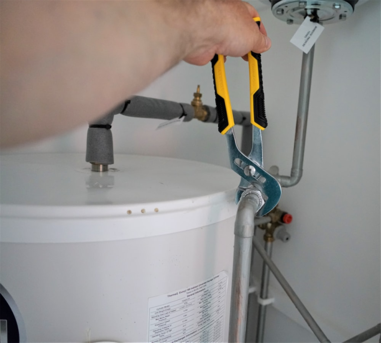 Plumber using a wrench to service a water heater's pipe fittings.