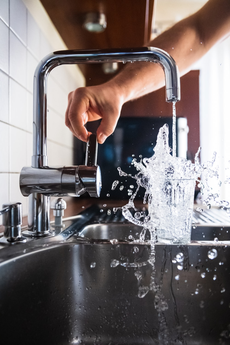 Hand running water at a kitchen sink faucet during a plumbing service call.