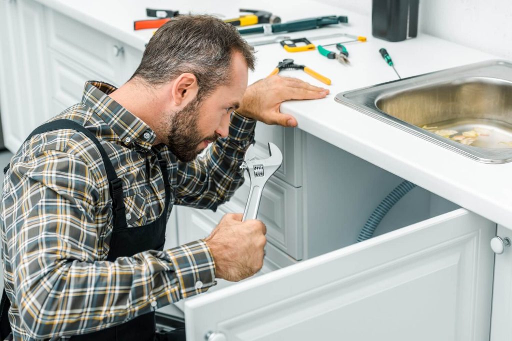 Plumber fixing a clogged, overflowing sink drain.