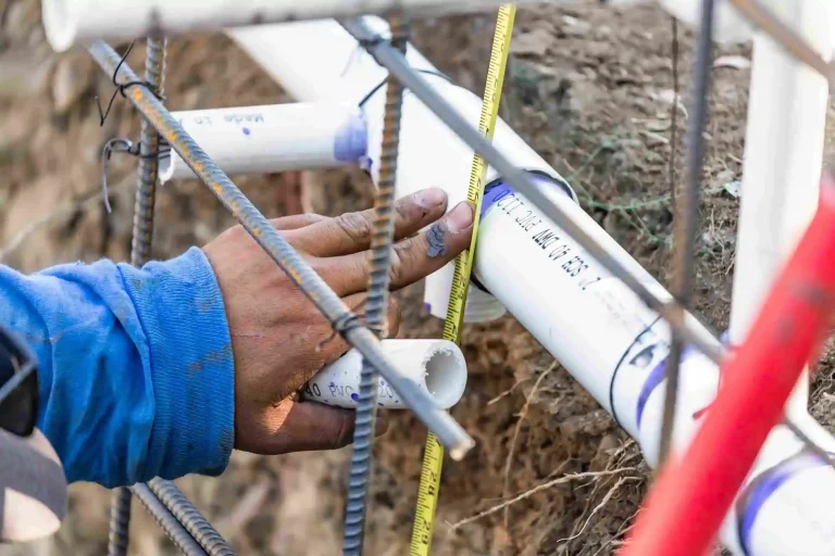Plumber using a tape measure while installing PVC pipe outdoors.