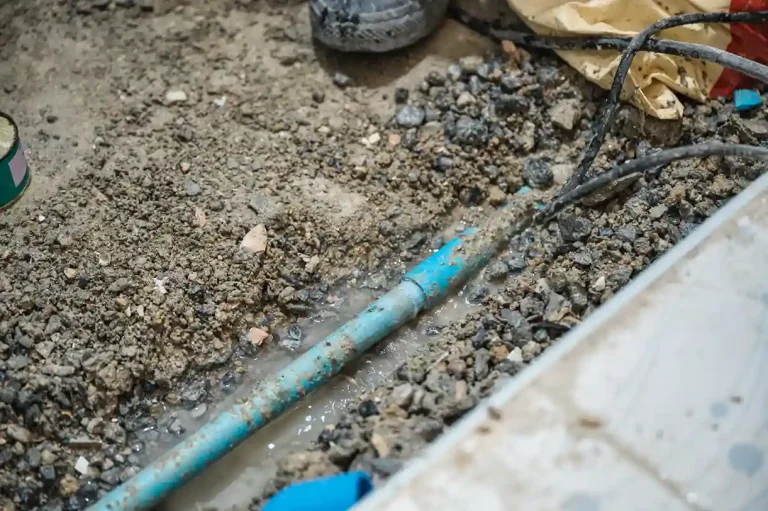 Plumber repairing a sewer pipe leak in an excavated trench.