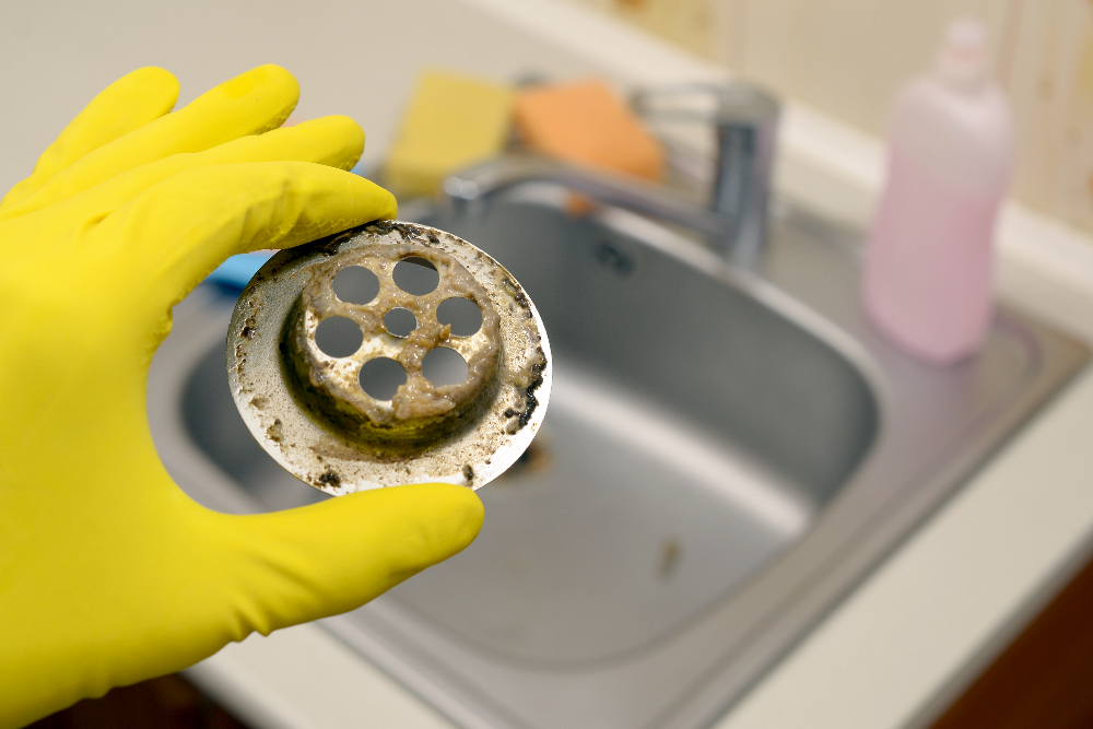 Plumber holding a drain strainer removed from a sink.