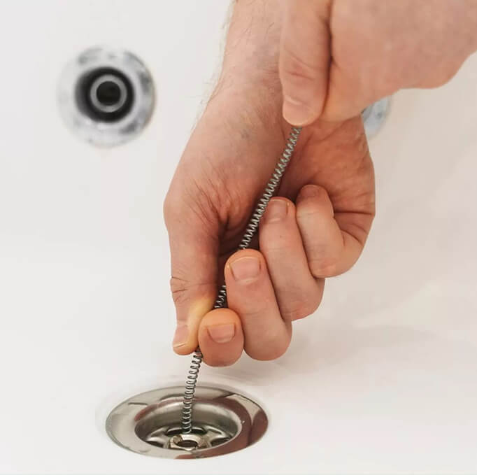 Plumber using a drain auger snake to clear a slow-draining bathtub drain.